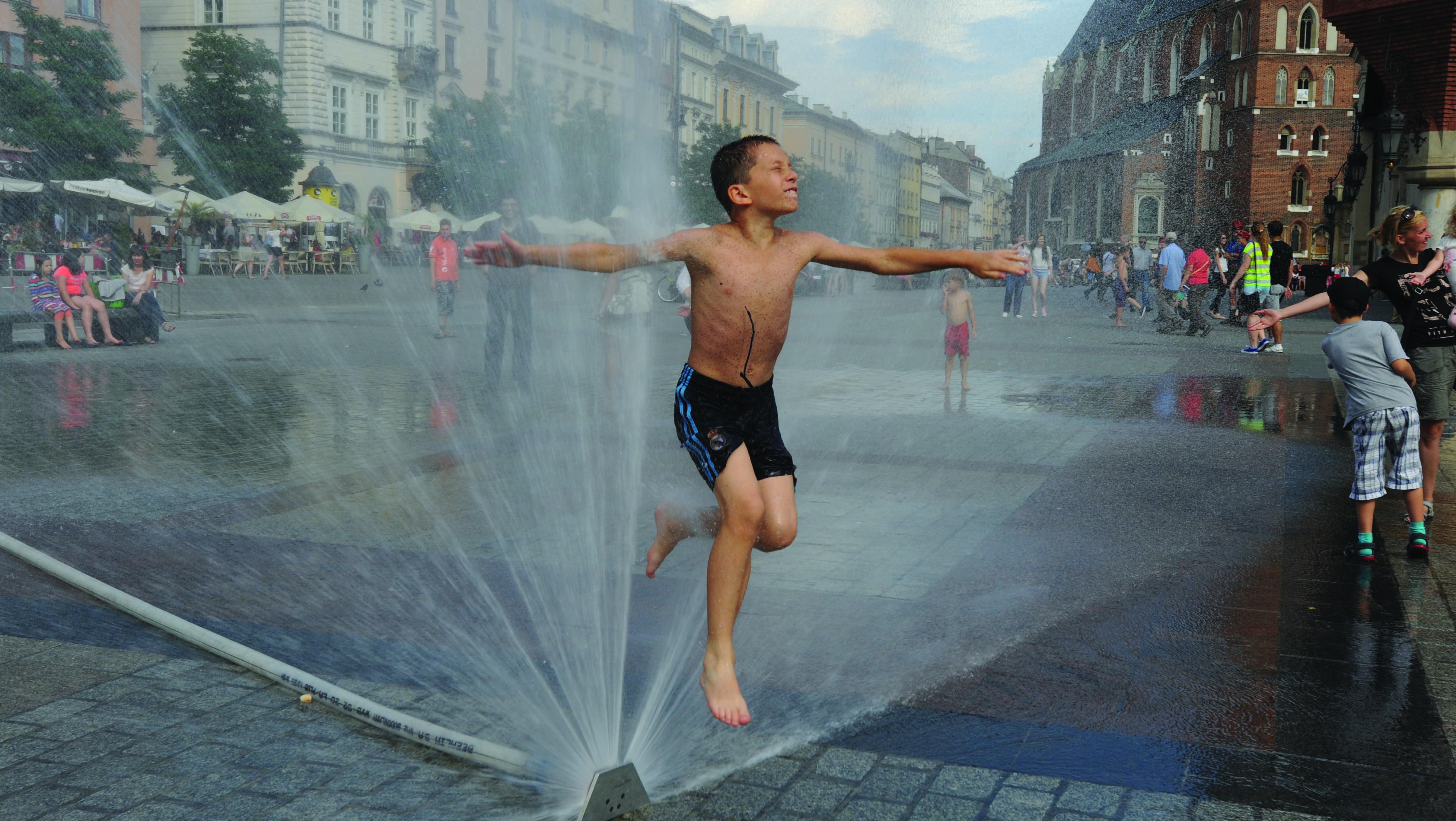 Fotografia na rua de criança em calções de banho a saltar por cima de repuxo